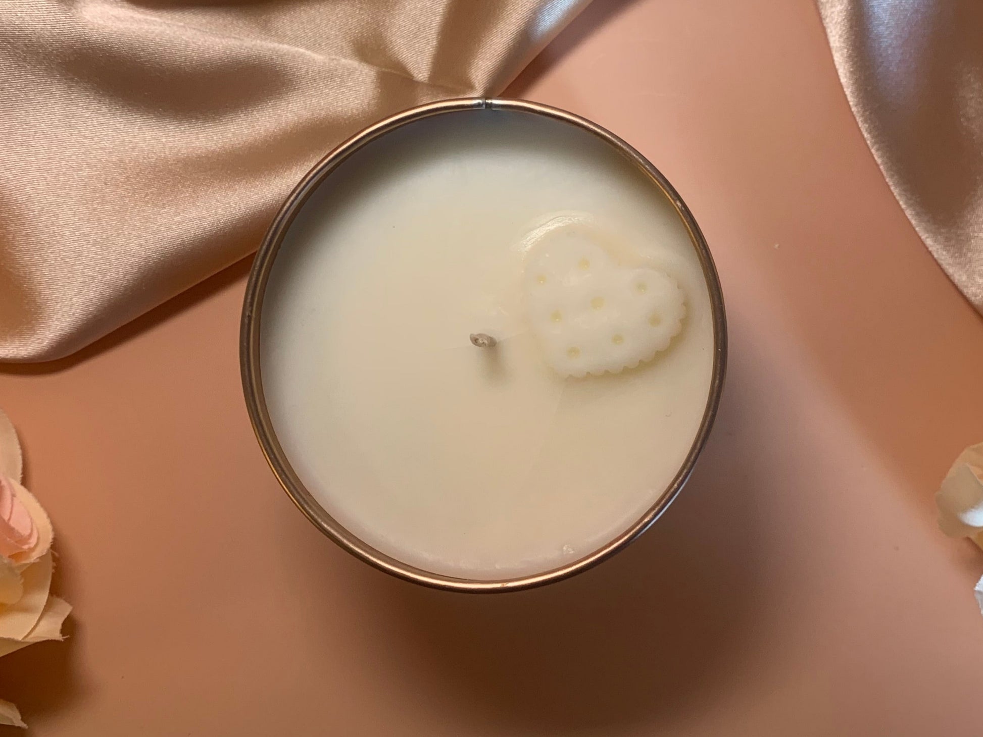 Candle in a tin with a decorative heart design on a soft pink background