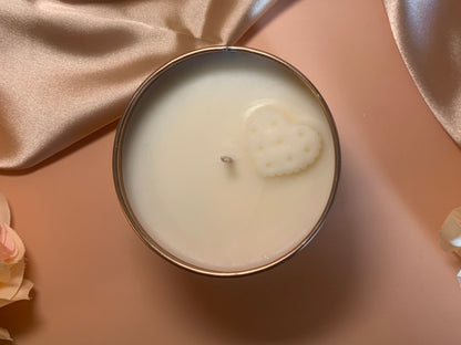 Candle in a tin with a decorative heart design on a soft pink background