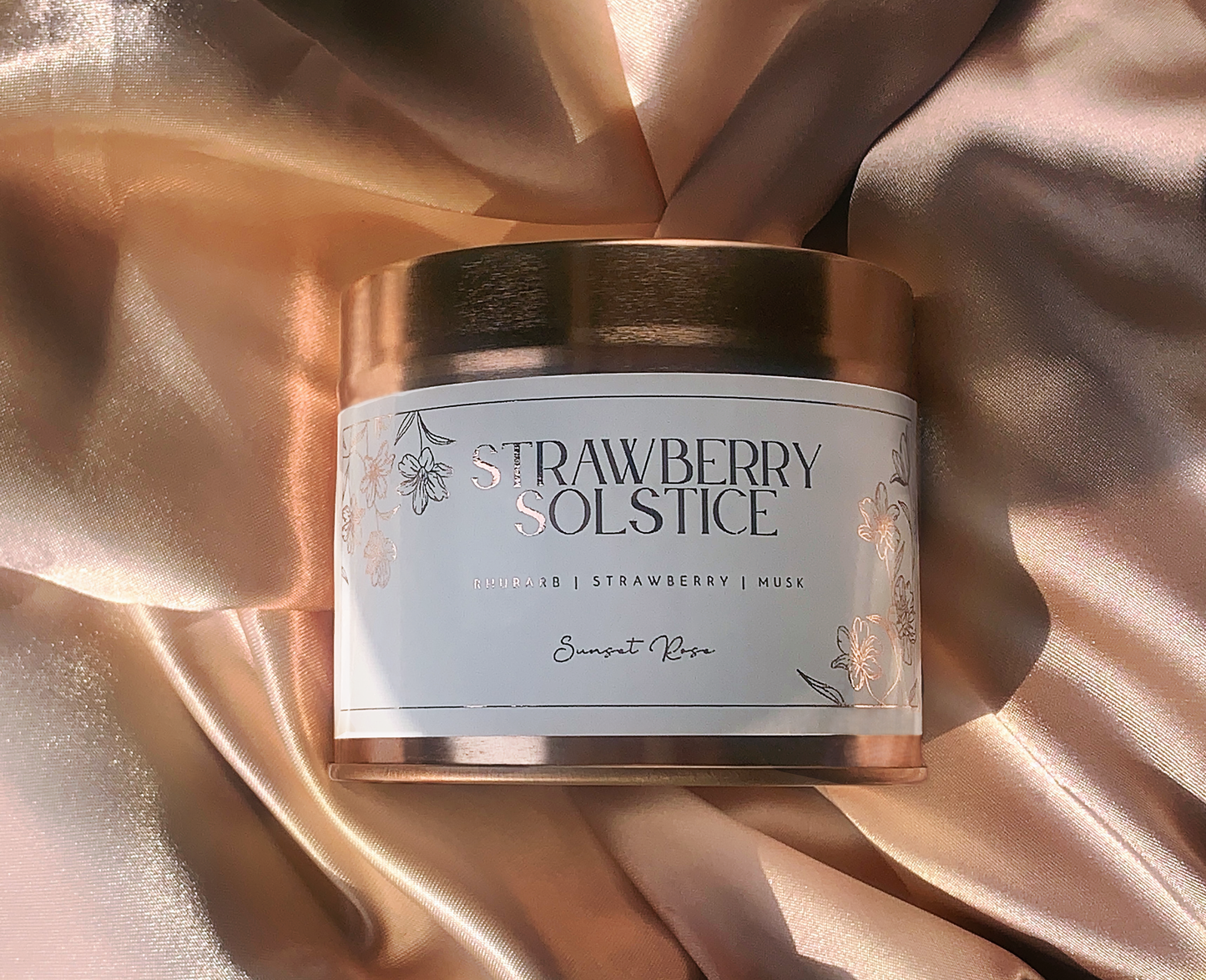 Candle tin labeled 'Strawberry Solstice' on a draped fabric background