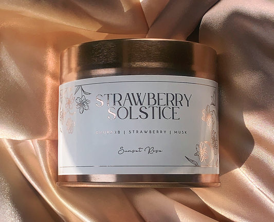 Candle tin labeled 'Strawberry Solstice' on a draped fabric background